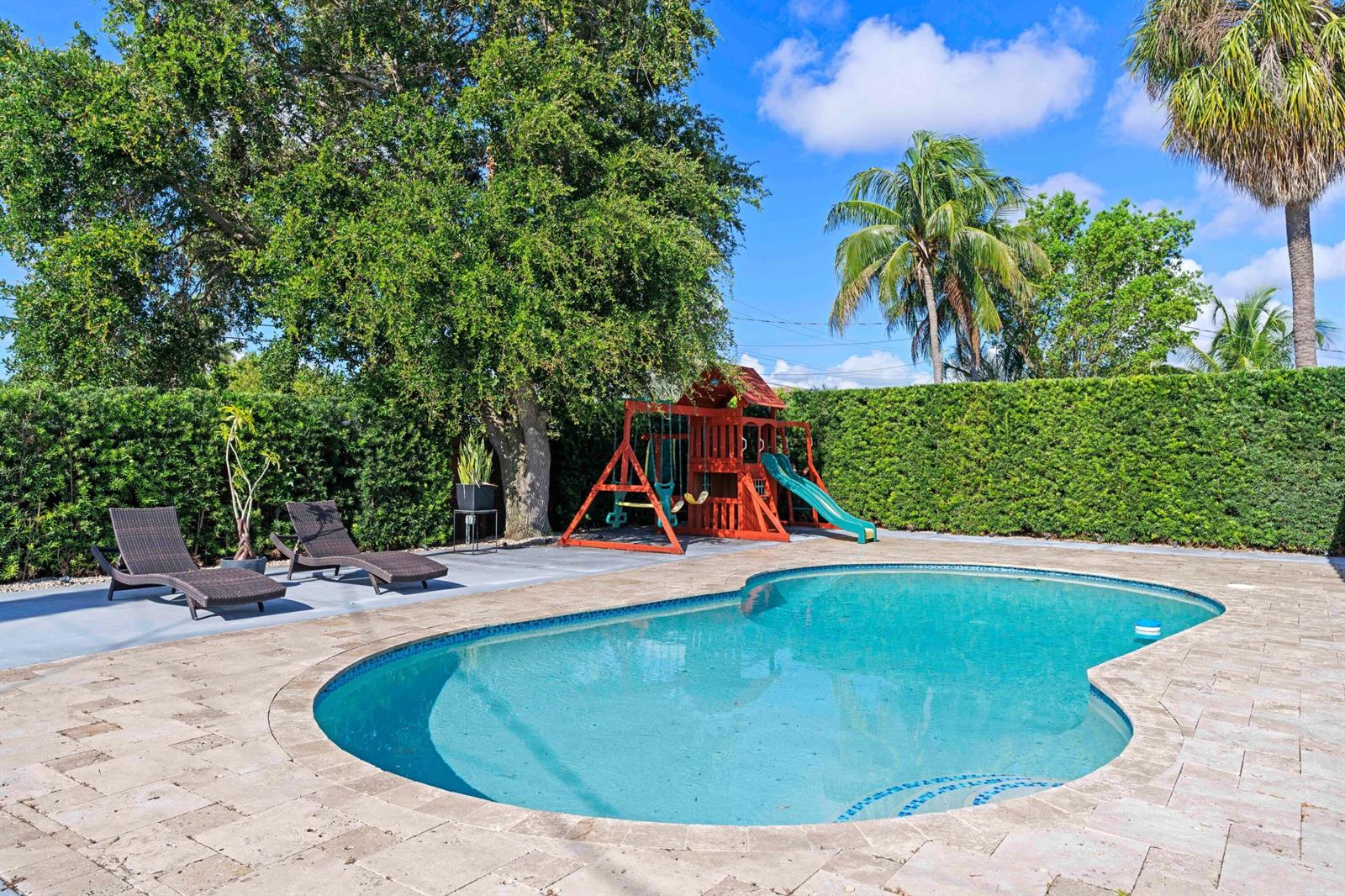 A backyard features a swimming pool, a wooden playset, and two lounge chairs on a patio — 300 SE 8th Court, Pompano Beach FL 33060, POMPANO BEACH, FL