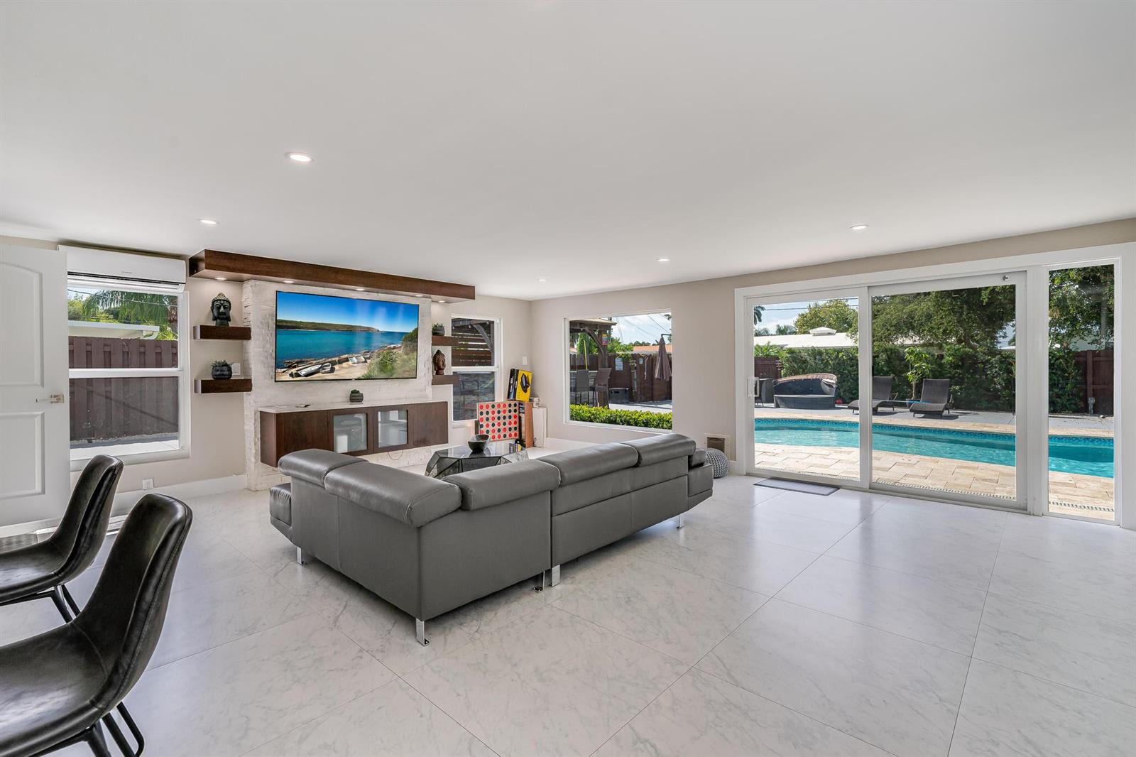 A living room features a grey sectional sofa, a wall-mounted television, and sliding glass doors — 300 SE 8th Court, Pompano Beach FL 33060, POMPANO BEACH, FL
