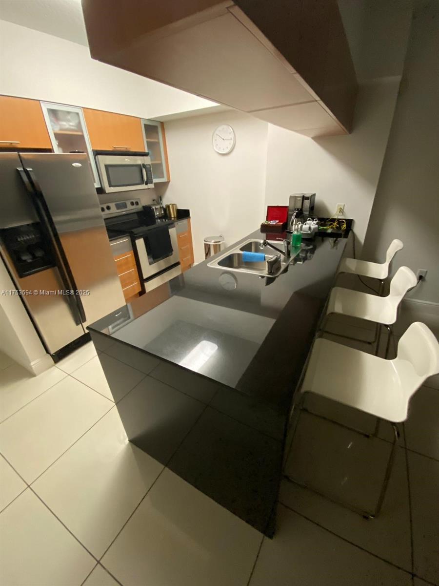 A kitchen features a black island with a sink, stainless steel appliances, and orange cabinetry — 1750 N Bayshore Dr # 2905, Miami FL 33132, MIAMI, FL