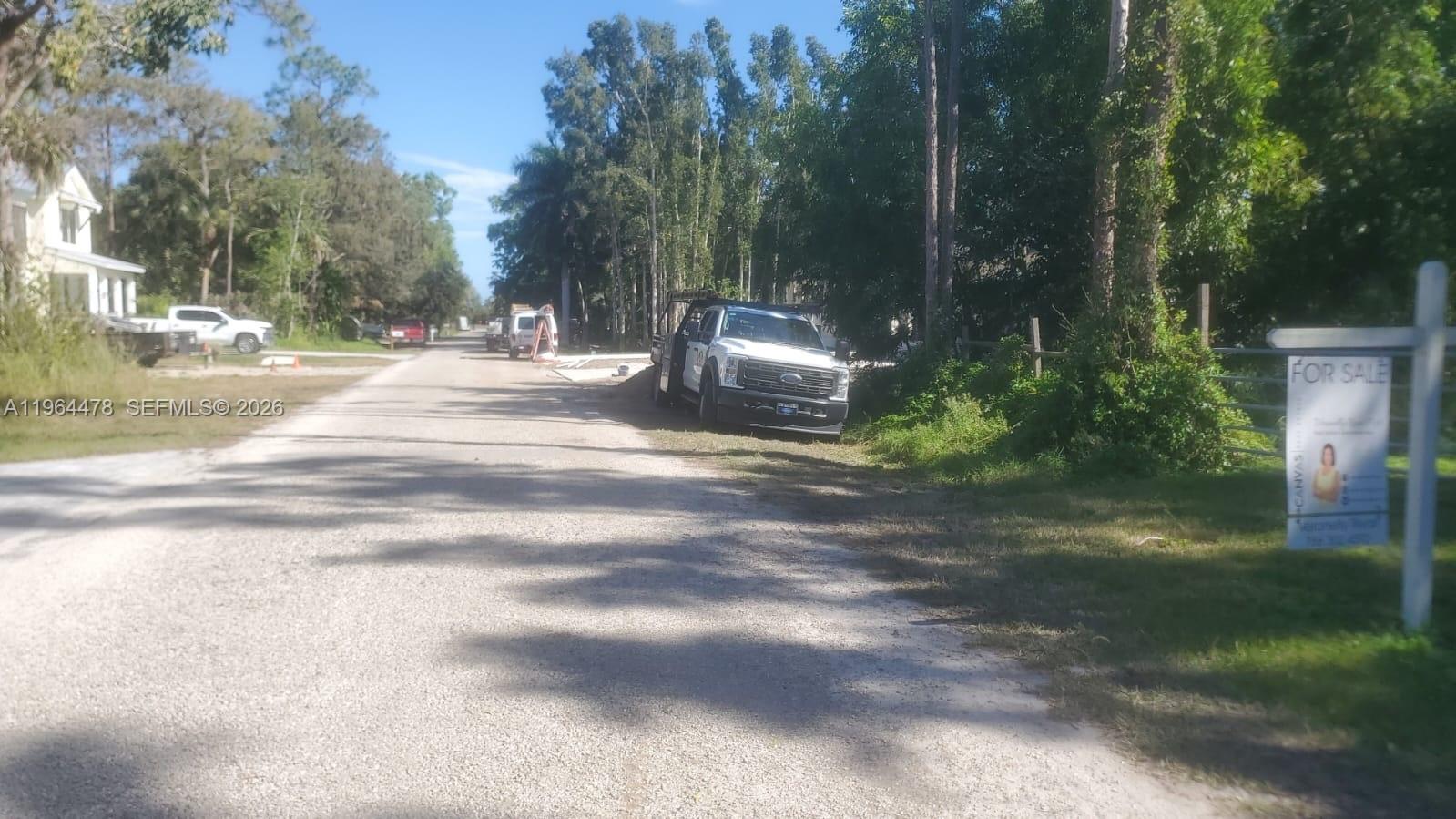 A gravel road leads past a white pickup truck and a for sale sign — 3050 Pine Tree Dr, Naples FL 34112, NAPLES, FL