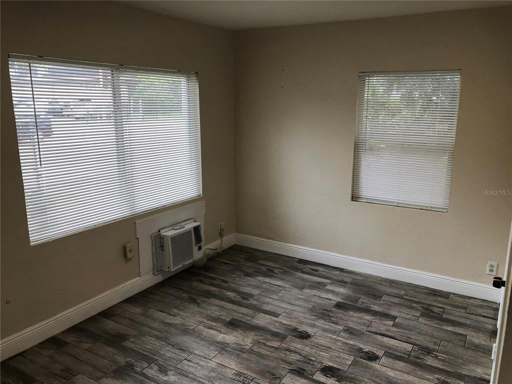An empty room features wood-look tile flooring, two windows with blinds, and a wall-mounted air conditioner — 7208 N NEBRASKA AVENUE UNIT 1, TAMPA, FL