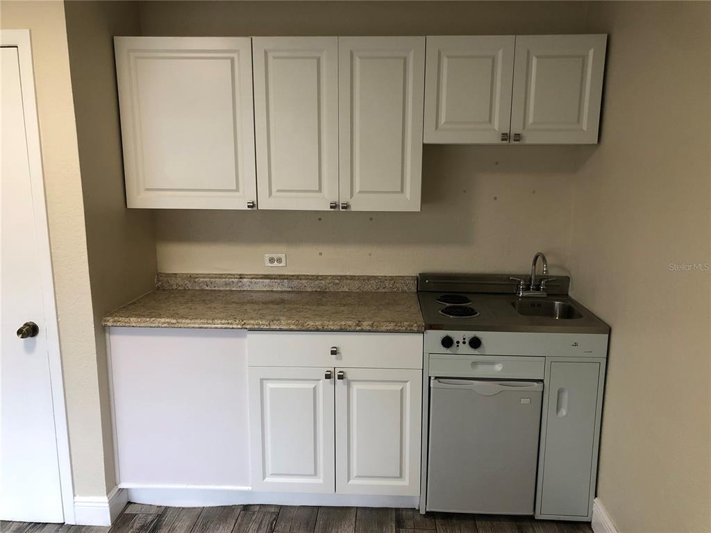 A small kitchenette features white cabinets, a stone-look countertop, a sink, and a compact stove — 7208 N NEBRASKA AVENUE UNIT 1, TAMPA, FL