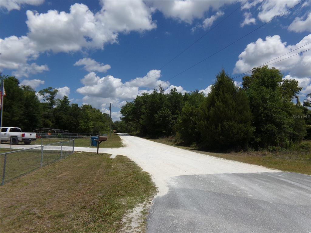 A gravel road transitions from a paved street, bordered by trees and a fenced property — KNOXVILLE DRIVE, WEBSTER, FL