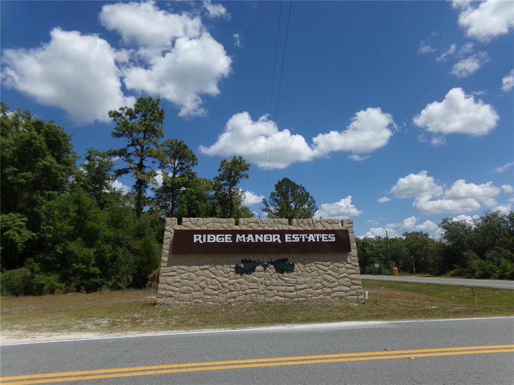 A stone monument sign for Ridge Manor Estates stands beside a road under a blue sky — KNOXVILLE DRIVE, WEBSTER, FL