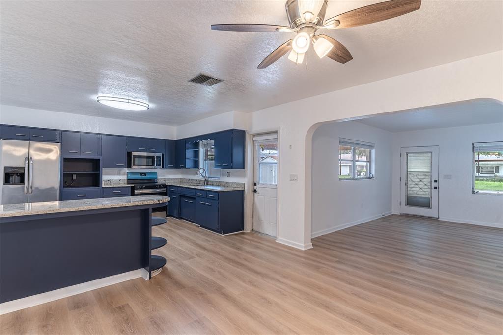 An open-concept kitchen and living area featuring navy blue cabinets, light wood flooring, and furniture — 145 BEVERLY DRIVE, WINTER HAVEN, FL