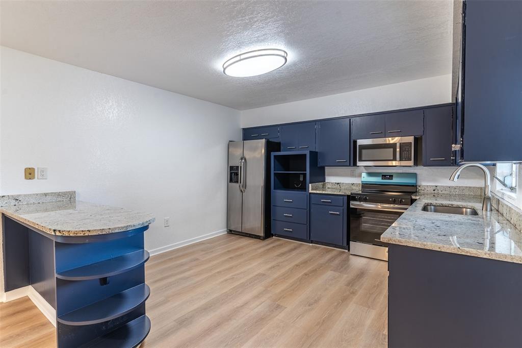 A kitchen features blue cabinets, granite countertops, stainless steel appliances, and light wood-look flooring — 145 BEVERLY DRIVE, WINTER HAVEN, FL