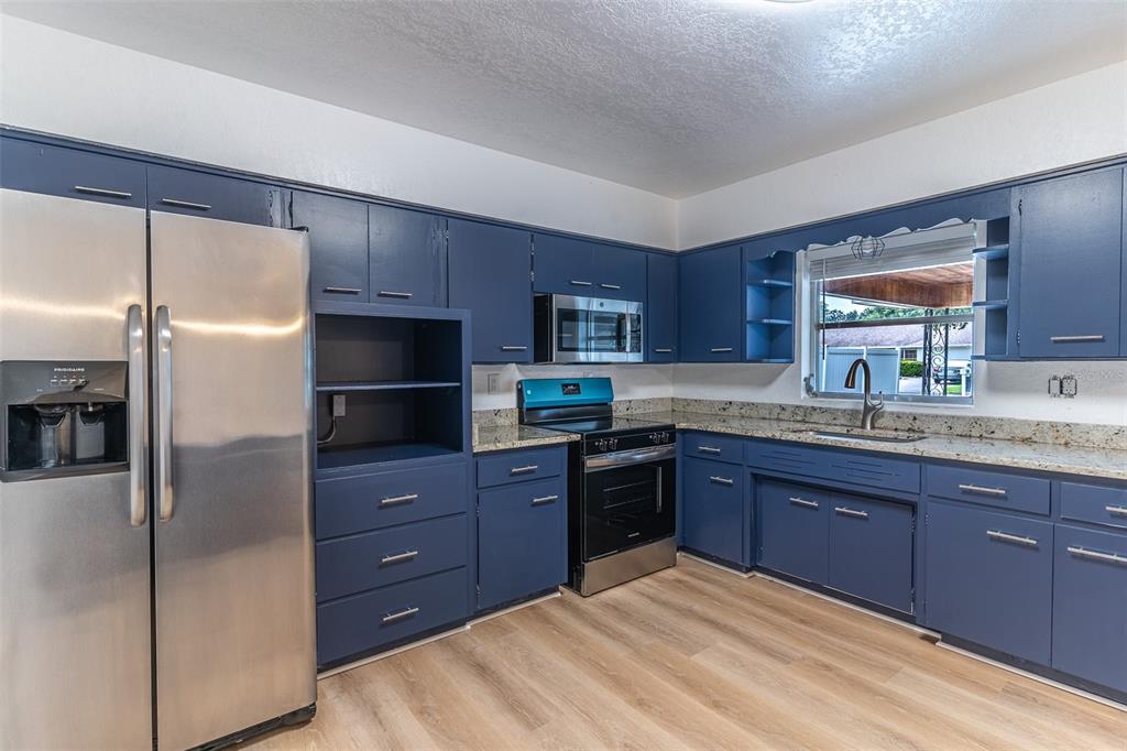 A kitchen features blue cabinets, stainless steel appliances, granite countertops, and light wood-look flooring — 145 BEVERLY DRIVE, WINTER HAVEN, FL