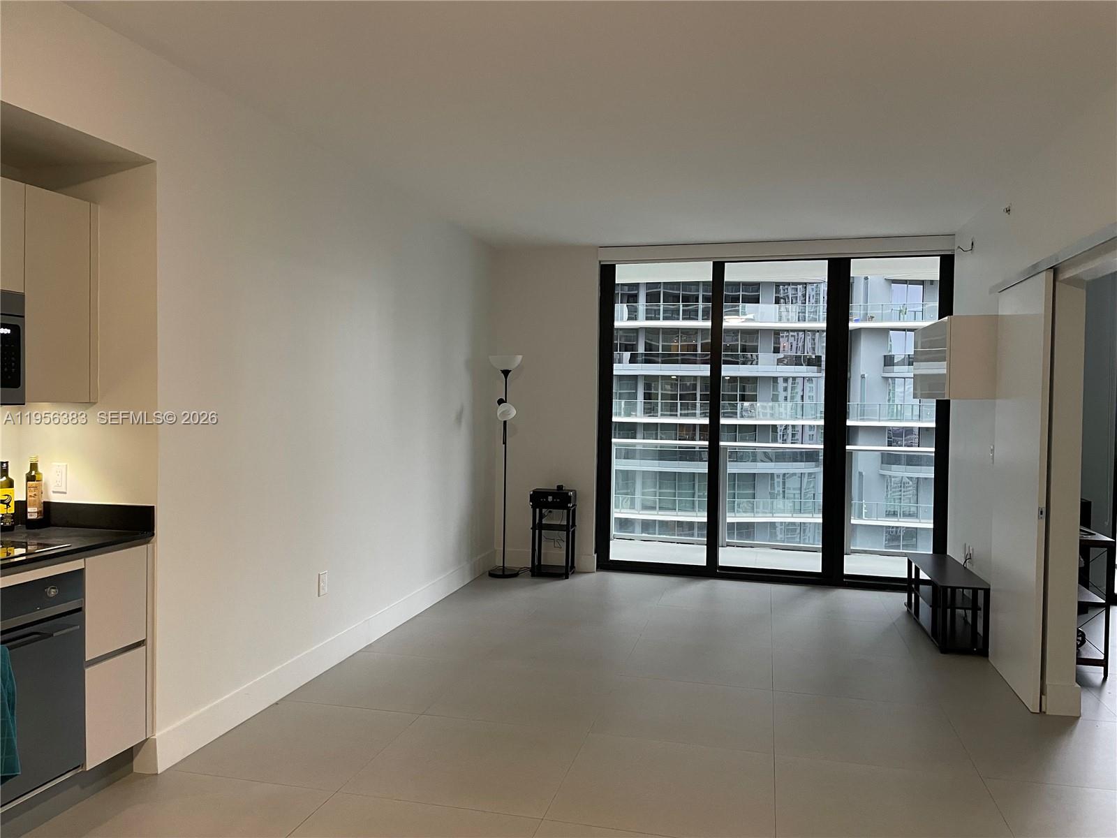 An unfurnished living area with large windows, light tile flooring, and an adjacent kitchen — 1010 Brickell Ave # 3708, Miami FL 33131, MIAMI, FL