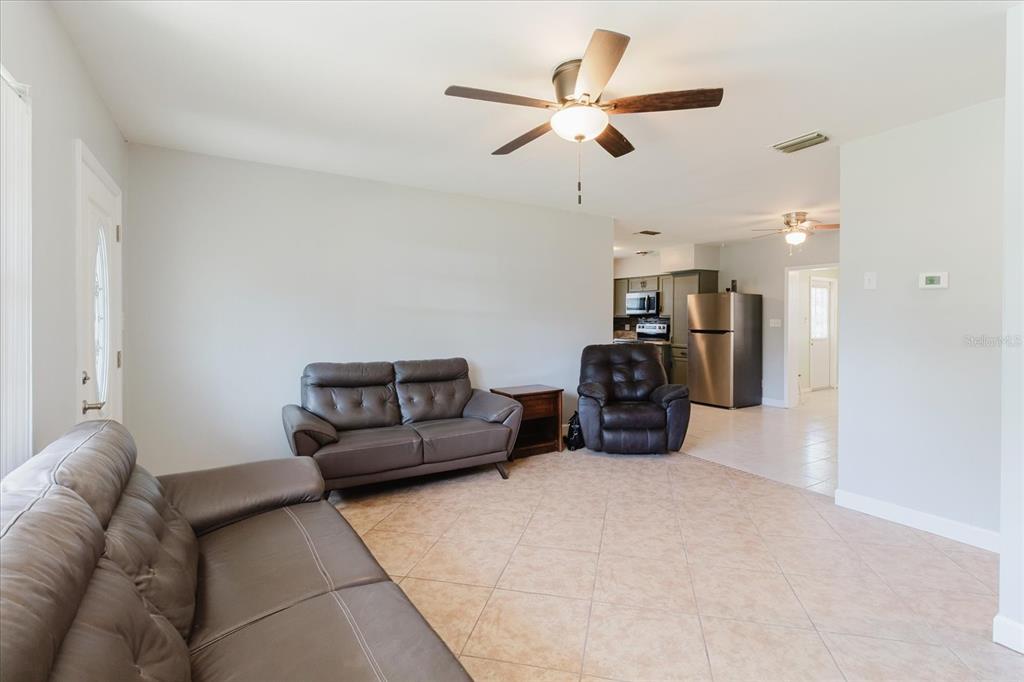 A living room with tile floors, leather furniture, and a ceiling fan opens to a kitchen — 6212 FLORIDA CIRCLE W, APOLLO BEACH, FL