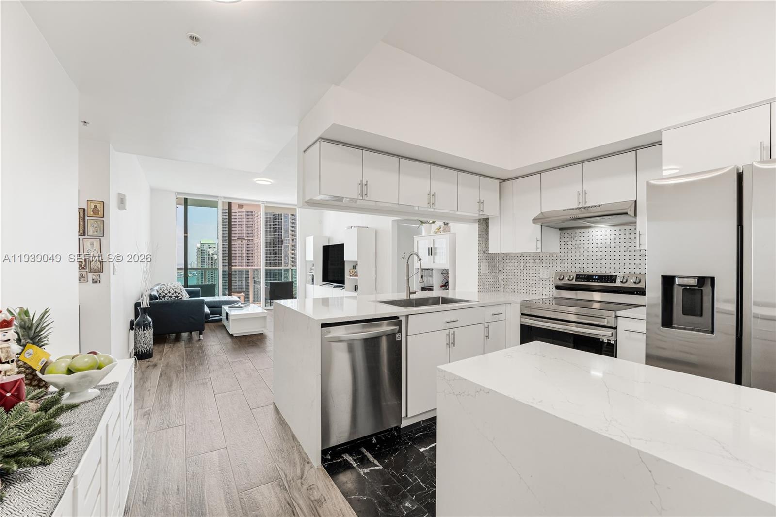A modern kitchen with white cabinets and quartz countertops overlooks a living area with balcony — 31 SE 5th St # 3918, Miami FL 33131, MIAMI, FL