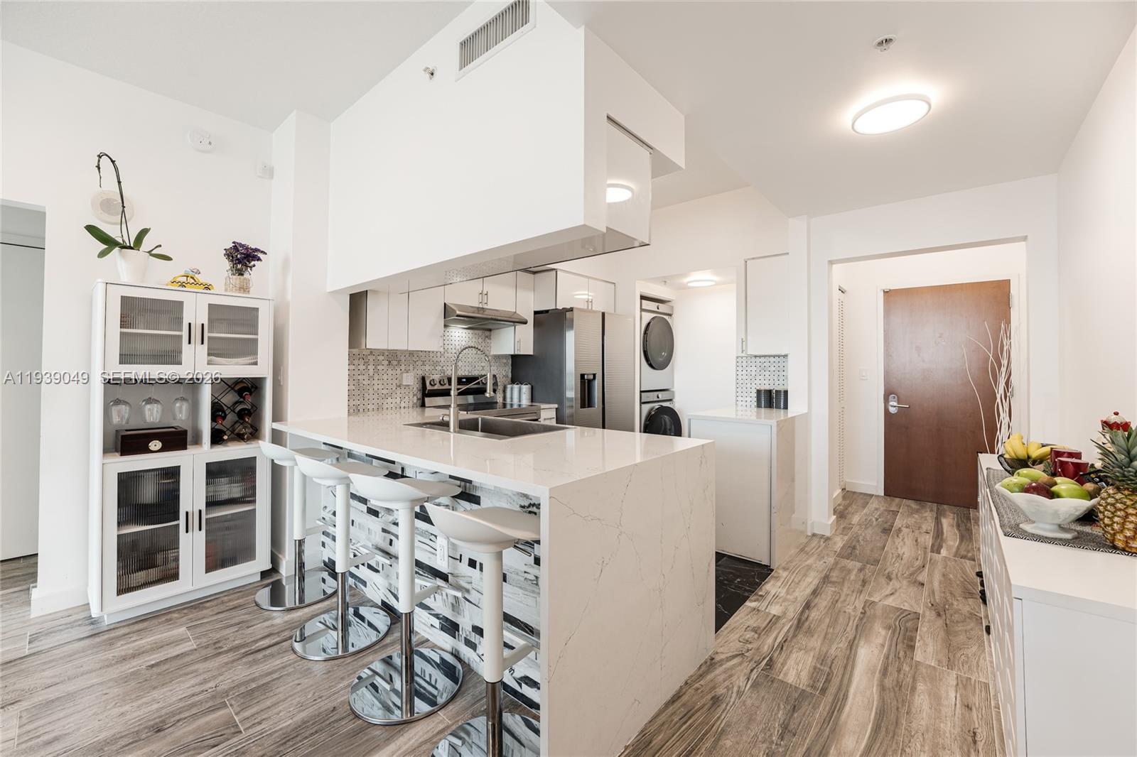 A modern kitchen features a white quartz island with bar stools and wood-look flooring — 31 SE 5th St # 3918, Miami FL 33131, MIAMI, FL