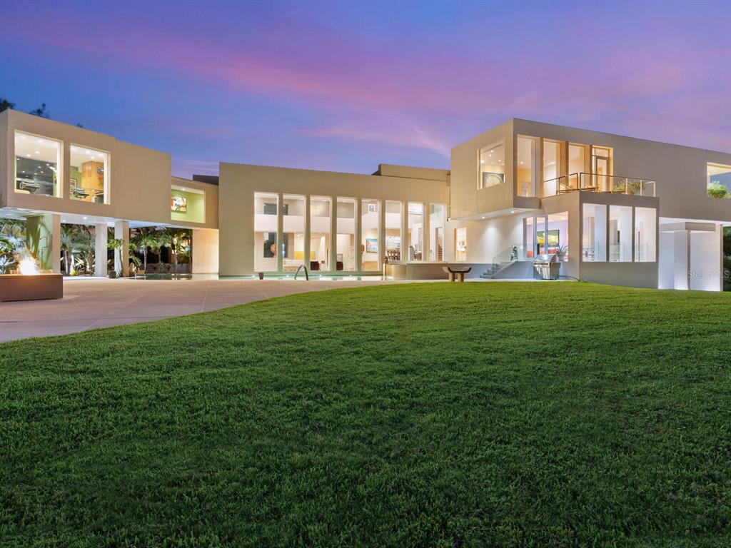 A modern multi-story house with large glass windows overlooks a grassy lawn at dusk — 6610 GULF OF MEXICO DRIVE, LONGBOAT KEY, FL