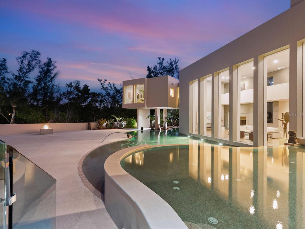 A modern house with a curved infinity pool and a cantilevered room at dusk — 6610 GULF OF MEXICO DRIVE, LONGBOAT KEY, FL