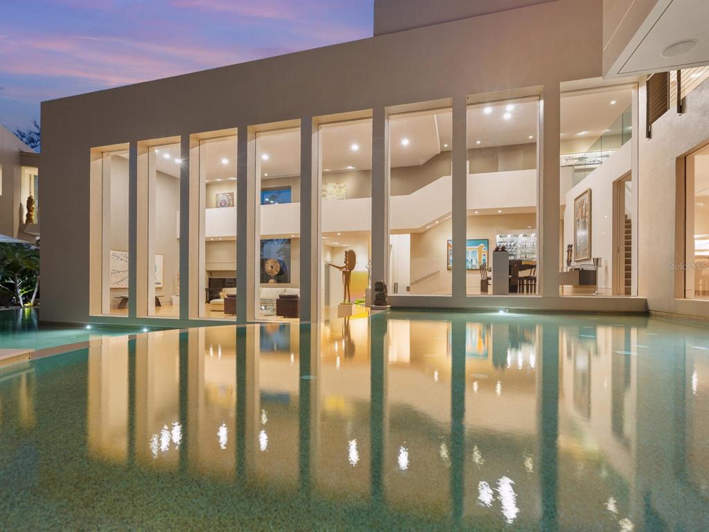 A modern house with floor-to-ceiling windows overlooks a calm swimming pool at twilight — 6610 GULF OF MEXICO DRIVE, LONGBOAT KEY, FL