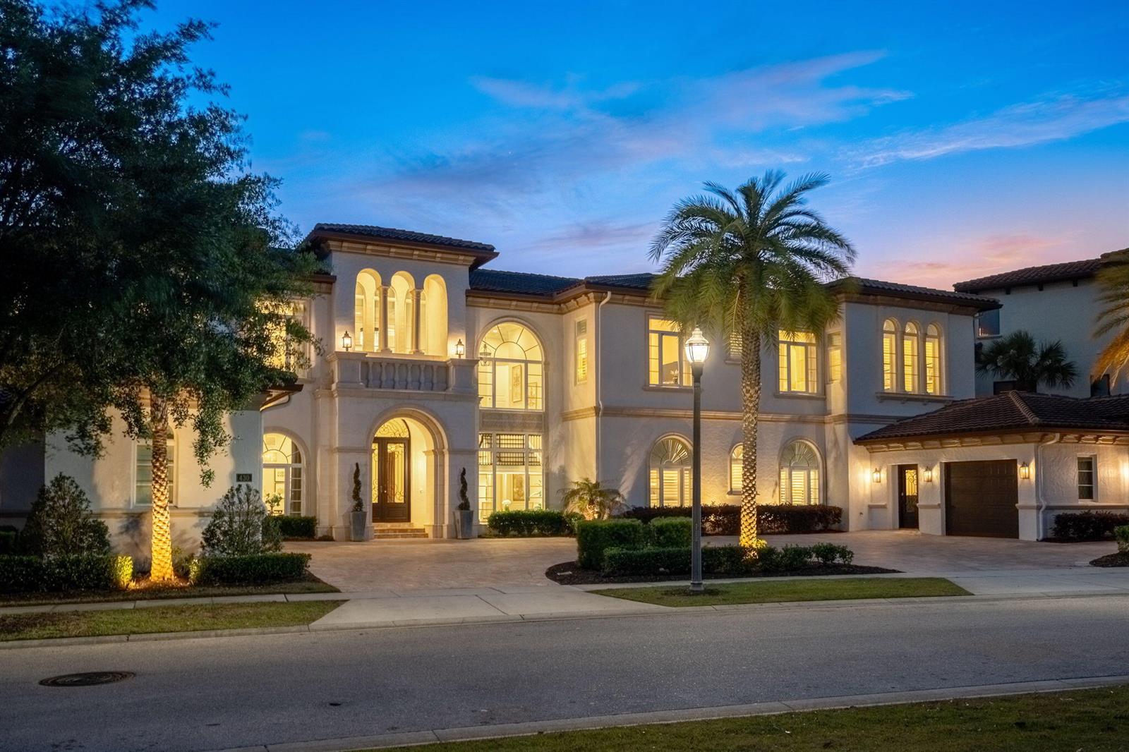 A two-story Mediterranean-style house with a paved driveway and palm trees at dusk — 430 Muirfield Loop, Kissimmee FL 34747, KISSIMMEE, FL