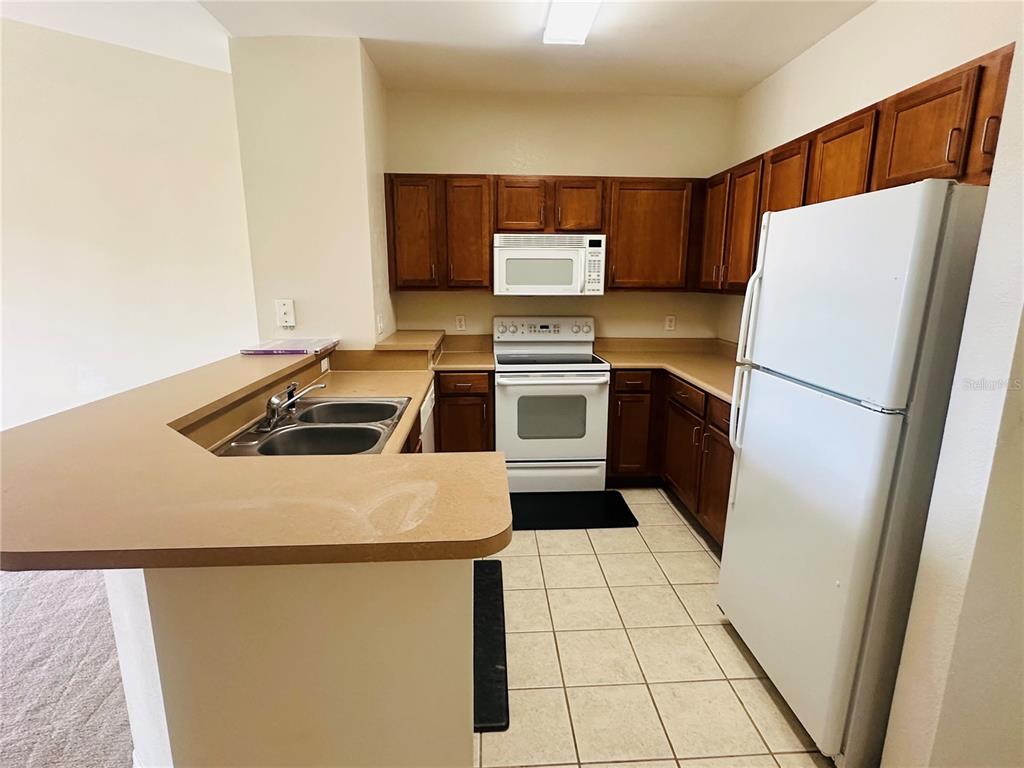 A kitchen features wood cabinets, white appliances, a double sink, and tan laminate countertops — 8124 CLAIRE ANN DRIVE UNIT 305, ORLANDO, FL