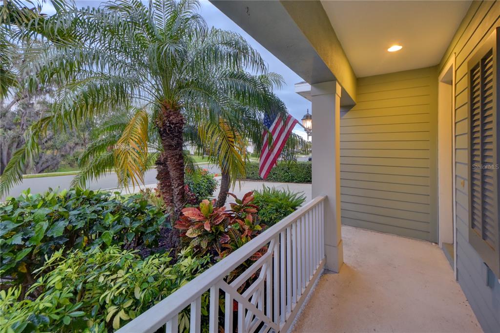A covered porch features a white railing, green siding, and a view of a palm tree — 7408 RIDGELAKE CIRCLE, BRADENTON, FL