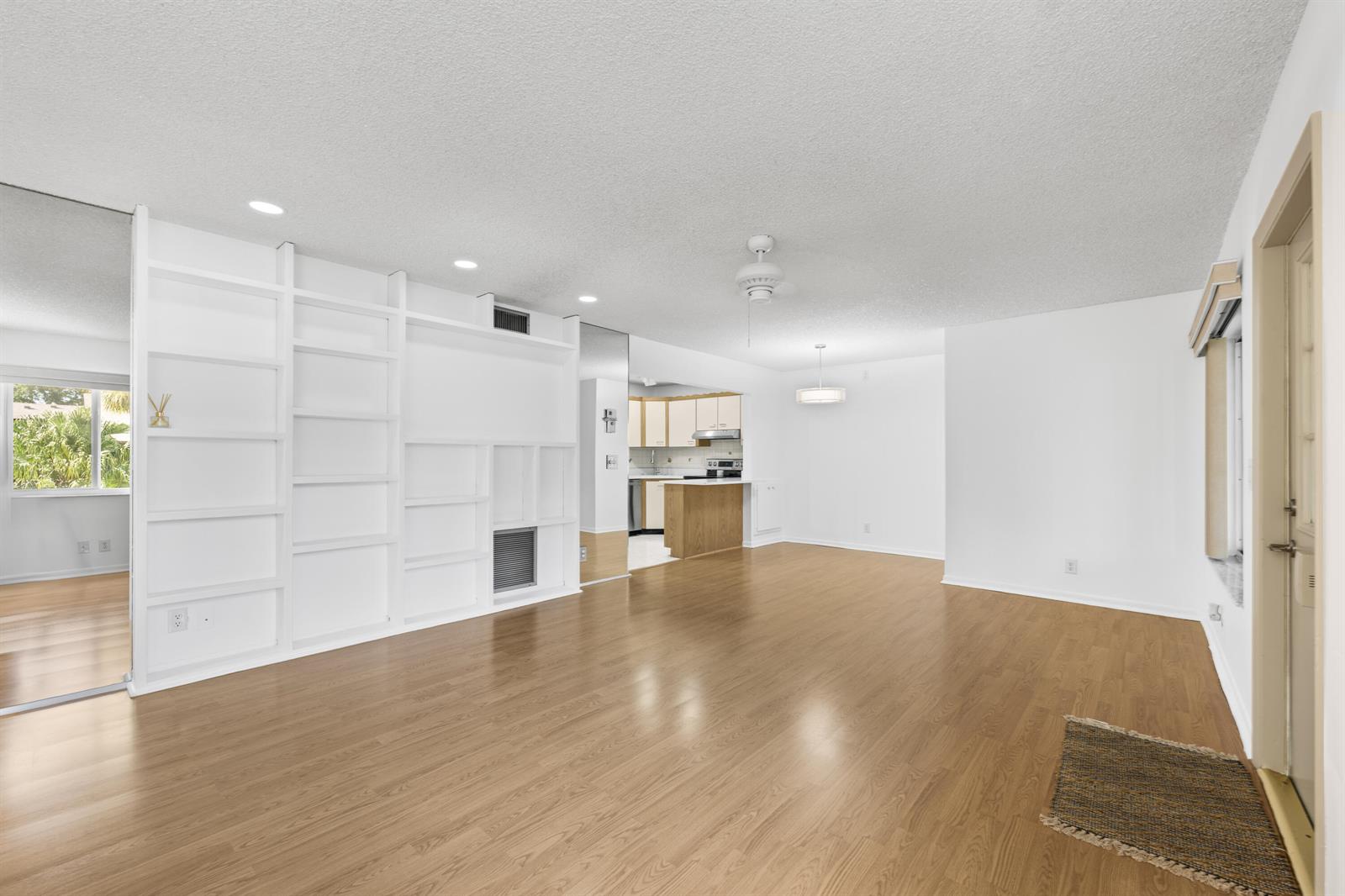 A bright living room features white built-in shelving, light wood-look flooring, and an adjacent kitchen — 313 Pine Ridge Circle # 2, FL 33463, FL