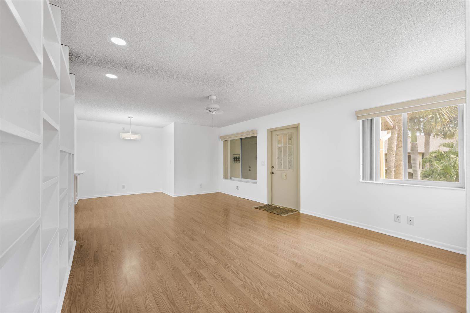 An empty living room features light wood flooring, white walls, built-in shelving, and a glass-paneled door — 313 Pine Ridge Circle # 2, FL 33463, FL