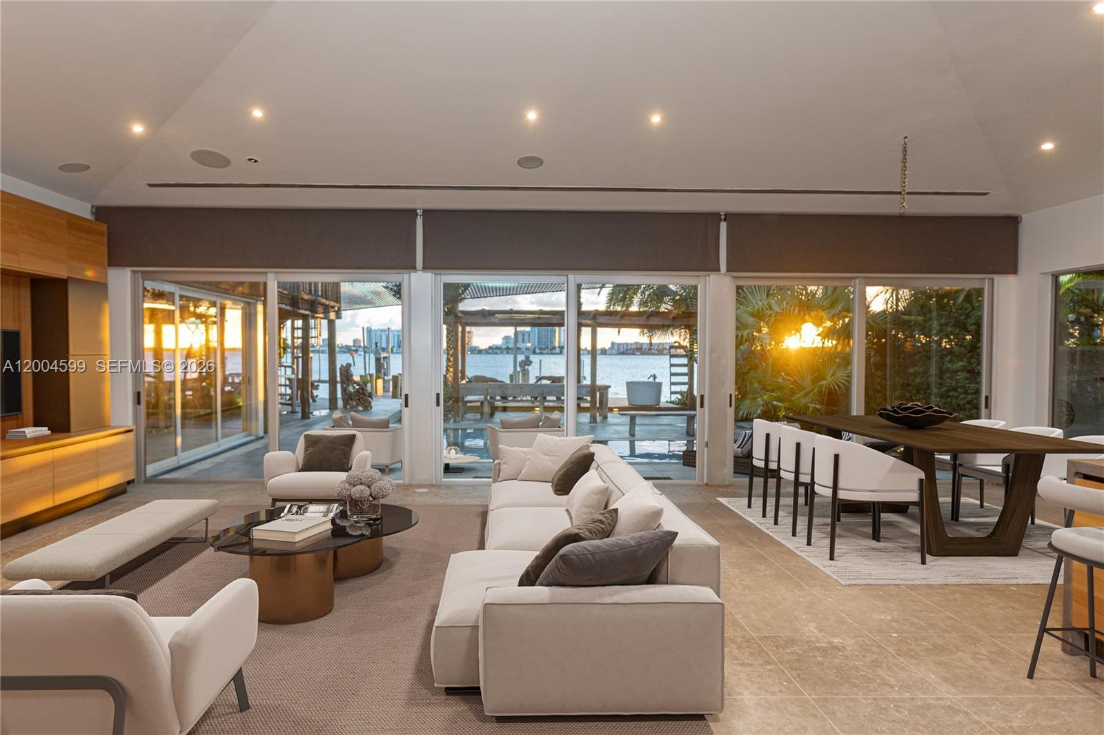 A modern living and dining area features floor-to-ceiling windows overlooking a waterfront patio — 2440 N Shore Ter, Miami Beach FL 33141, MIAMI BEACH, FL
