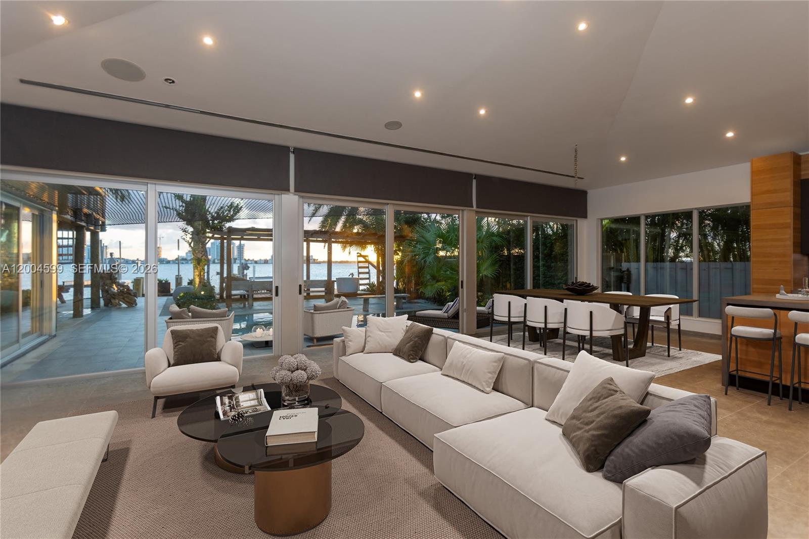 A modern living and dining area features floor-to-ceiling glass doors overlooking a waterfront patio — 2440 N Shore Ter, Miami Beach FL 33141, MIAMI BEACH, FL
