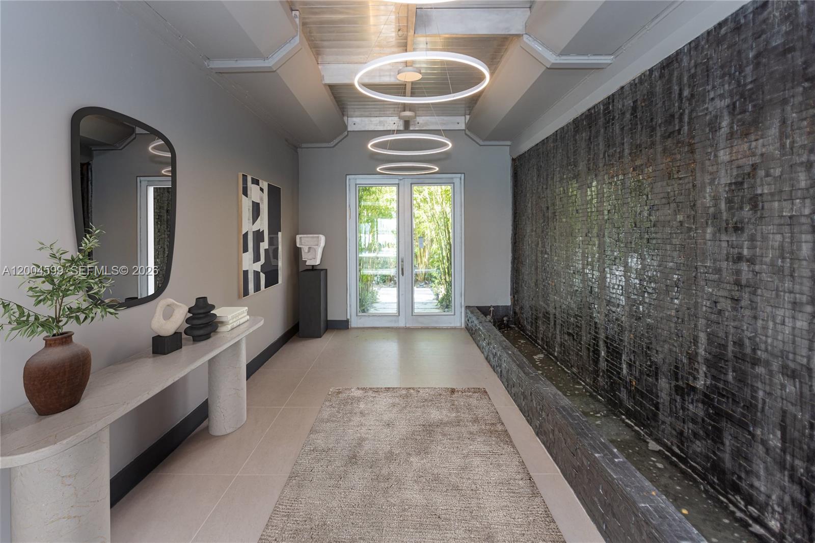 A modern entryway features a stone water wall, circular pendant lights, and a console table — 2440 N Shore Ter, Miami Beach FL 33141, MIAMI BEACH, FL