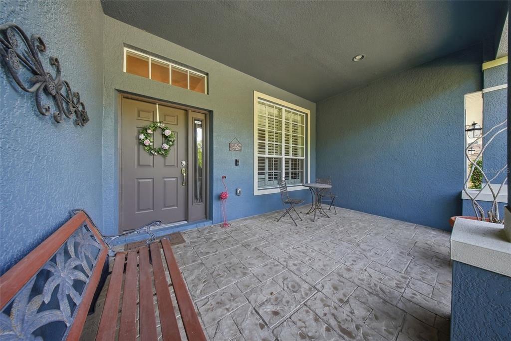 A covered front porch features a brown door, a bench, and a small bistro set — 7544 WHISPERING WIND DRIVE, LAND O LAKES, FL