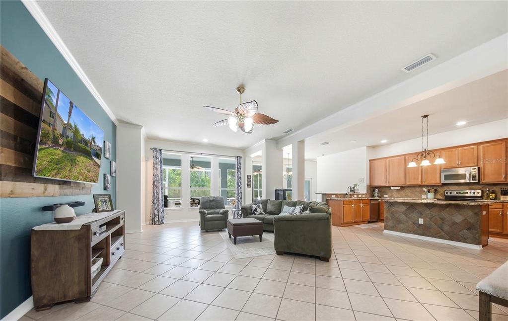 An open-concept living room with tile floors, a ceiling fan, and an adjacent kitchen — 7544 WHISPERING WIND DRIVE, LAND O LAKES, FL