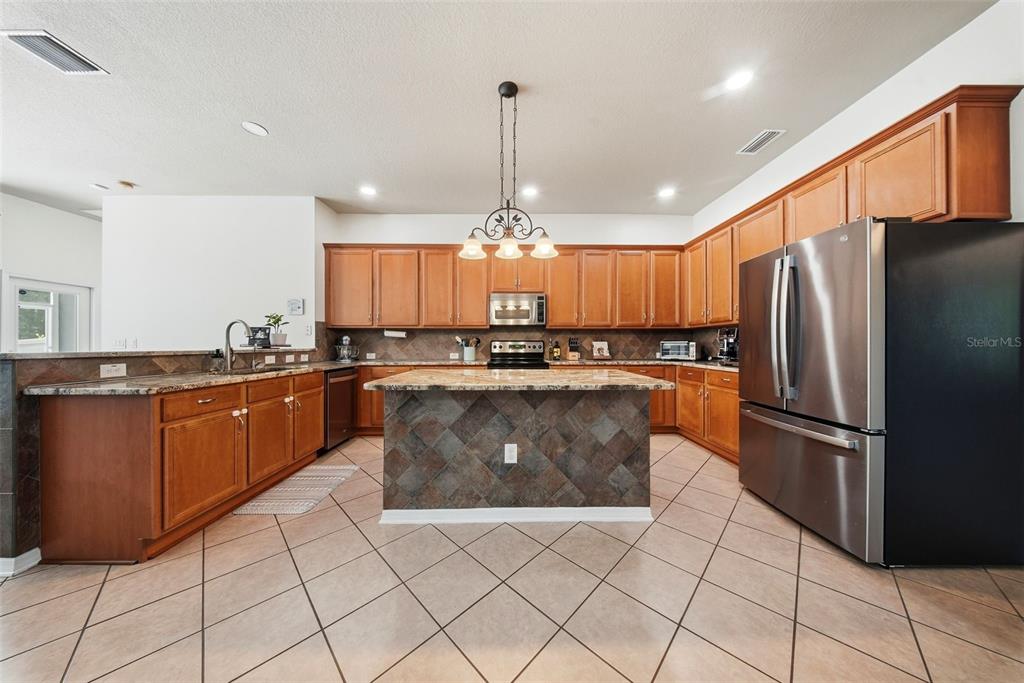 A kitchen features wood cabinets, granite countertops, a central island, and tile flooring — 7544 WHISPERING WIND DRIVE, LAND O LAKES, FL