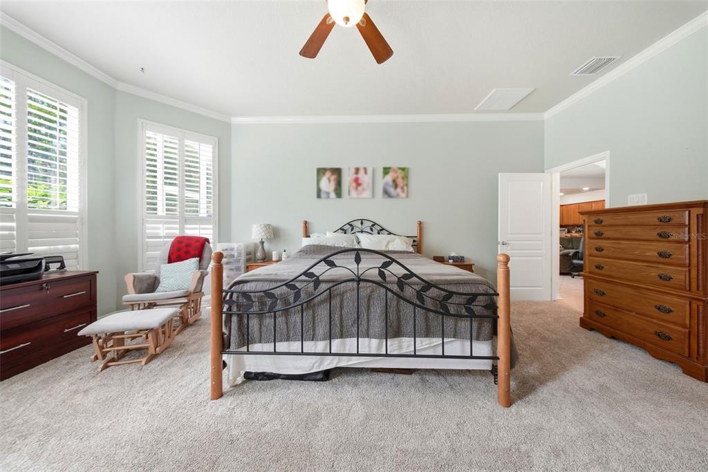 A bedroom features a metal-framed bed, a wooden dresser, a rocking chair, and carpeted floors — 7544 WHISPERING WIND DRIVE, LAND O LAKES, FL
