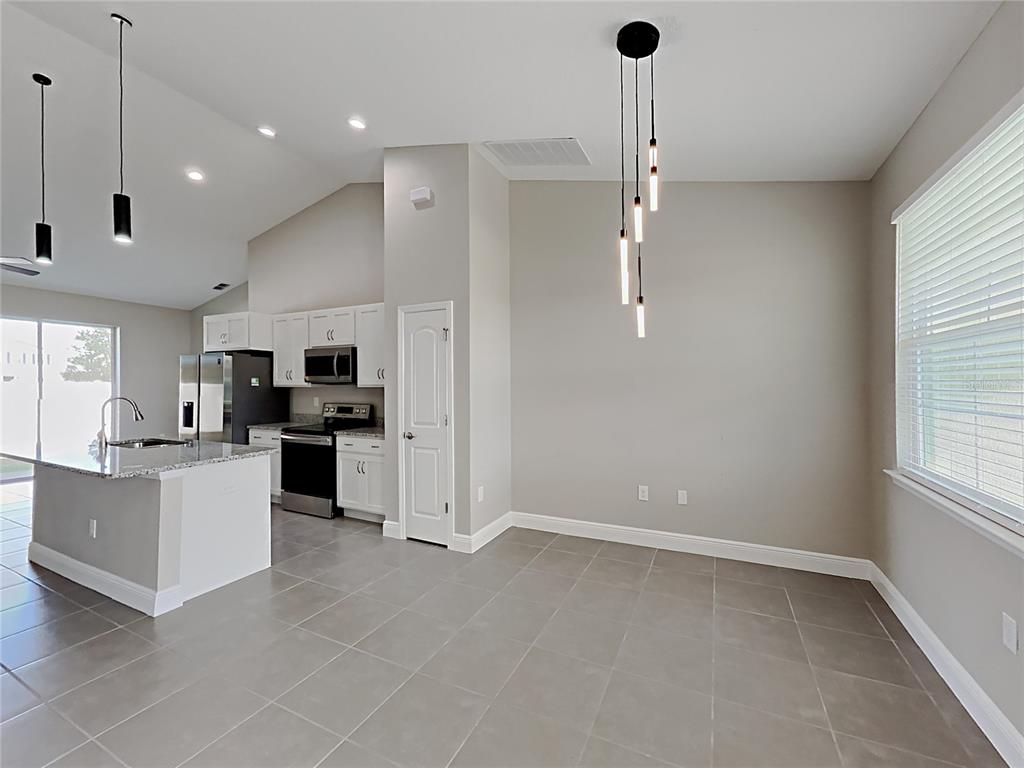 A kitchen with a granite-topped island and stainless steel appliances opens to a dining area — 309 FERN COURT, KISSIMMEE, FL