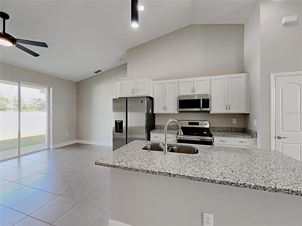 A kitchen with white cabinets, granite countertops, stainless steel appliances, and tile flooring — 309 FERN COURT, KISSIMMEE, FL