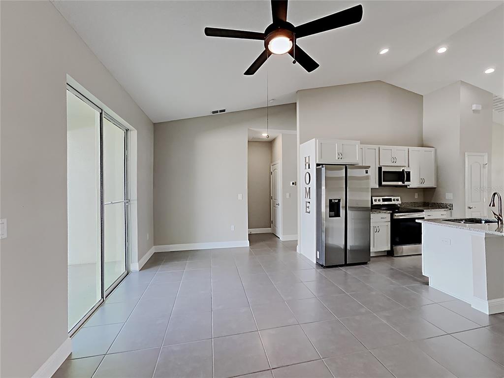 A kitchen with stainless steel appliances and white cabinets opens to a tiled living area — 309 FERN COURT, KISSIMMEE, FL