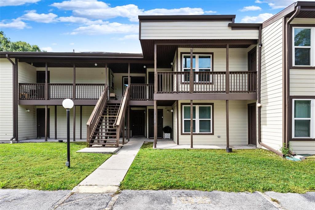 A two-story apartment building with beige siding, brown trim, and an exterior wooden staircase — 23202 SANDALWOOD DRIVE UNIT 202, WILDWOOD, FL