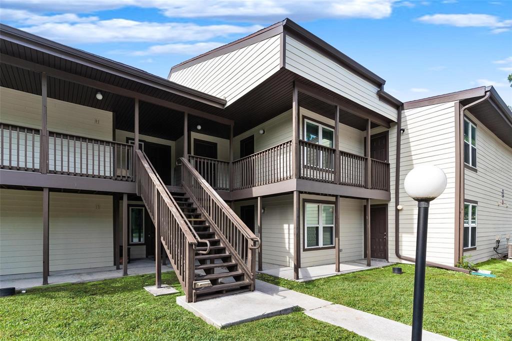 A two-story apartment building features exterior wooden staircases, balconies, and light-colored horizontal siding — 23202 SANDALWOOD DRIVE UNIT 202, WILDWOOD, FL