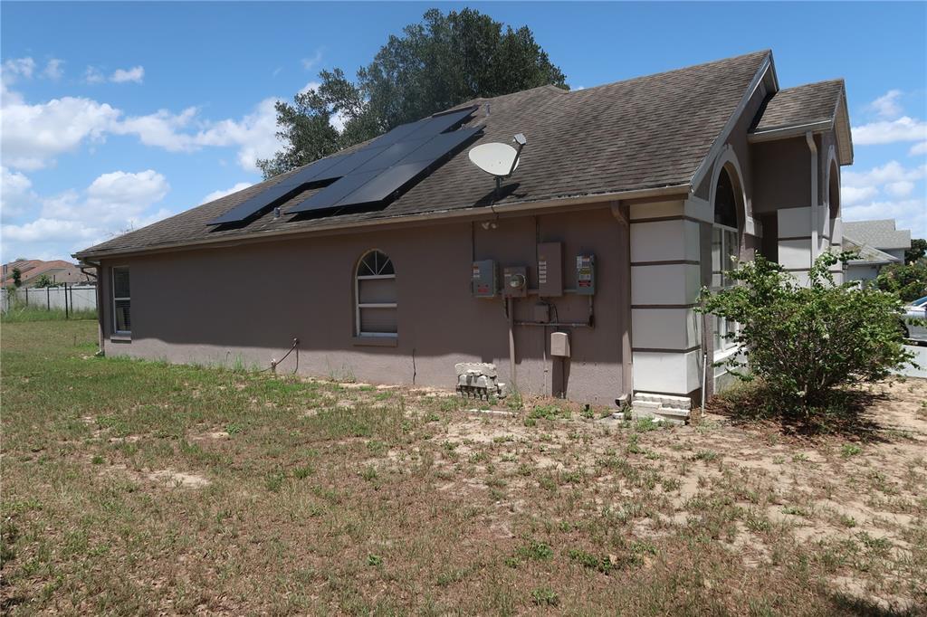 The exterior side of a house features solar panels on the roof and electrical equipment — 7337 HIGH LAKE DRIVE, ORLANDO, FL
