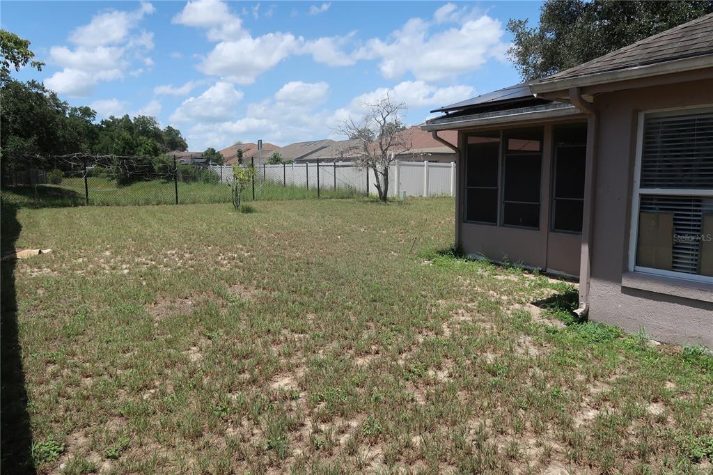 A grassy backyard features a screened-in patio attached to the side of a house — 7337 HIGH LAKE DRIVE, ORLANDO, FL