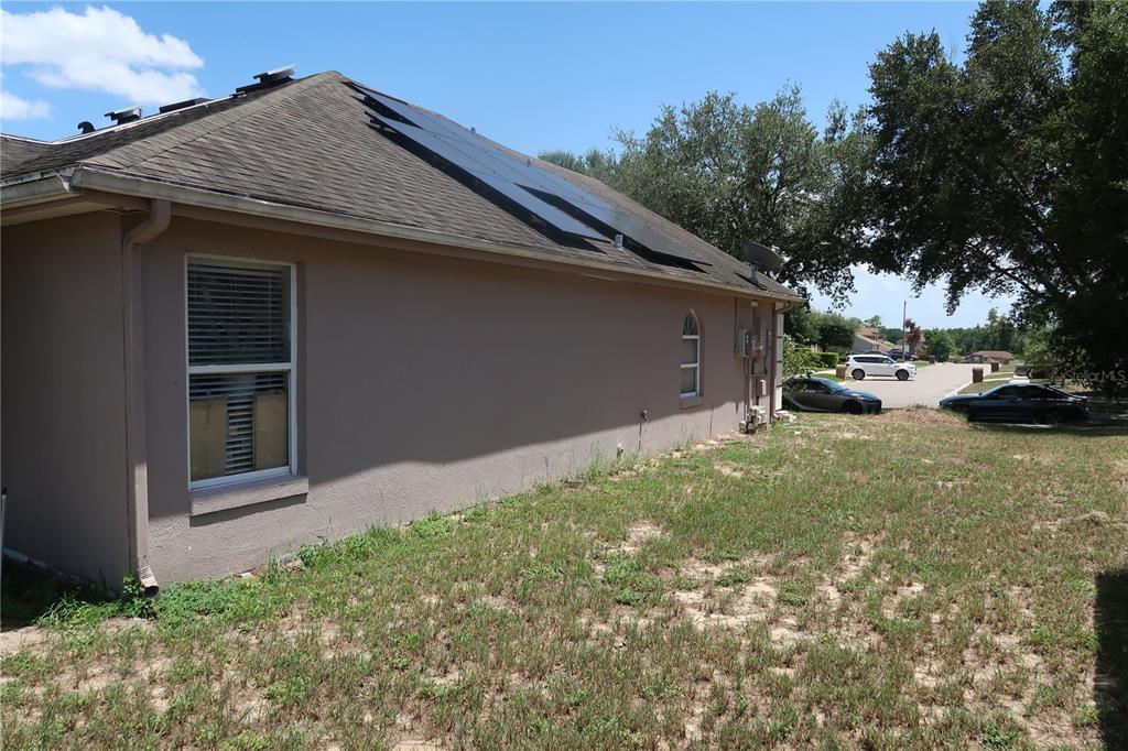 The side exterior of a house features a tan stucco wall, a window, and roof-mounted solar panels — 7337 HIGH LAKE DRIVE, ORLANDO, FL
