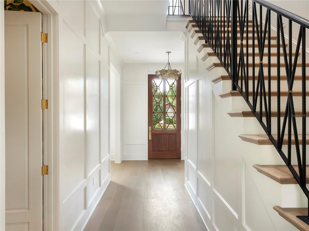 A bright entryway features white paneled walls, light wood flooring, and a black metal staircase — 541 W CANTON AVENUE, WINTER PARK, FL