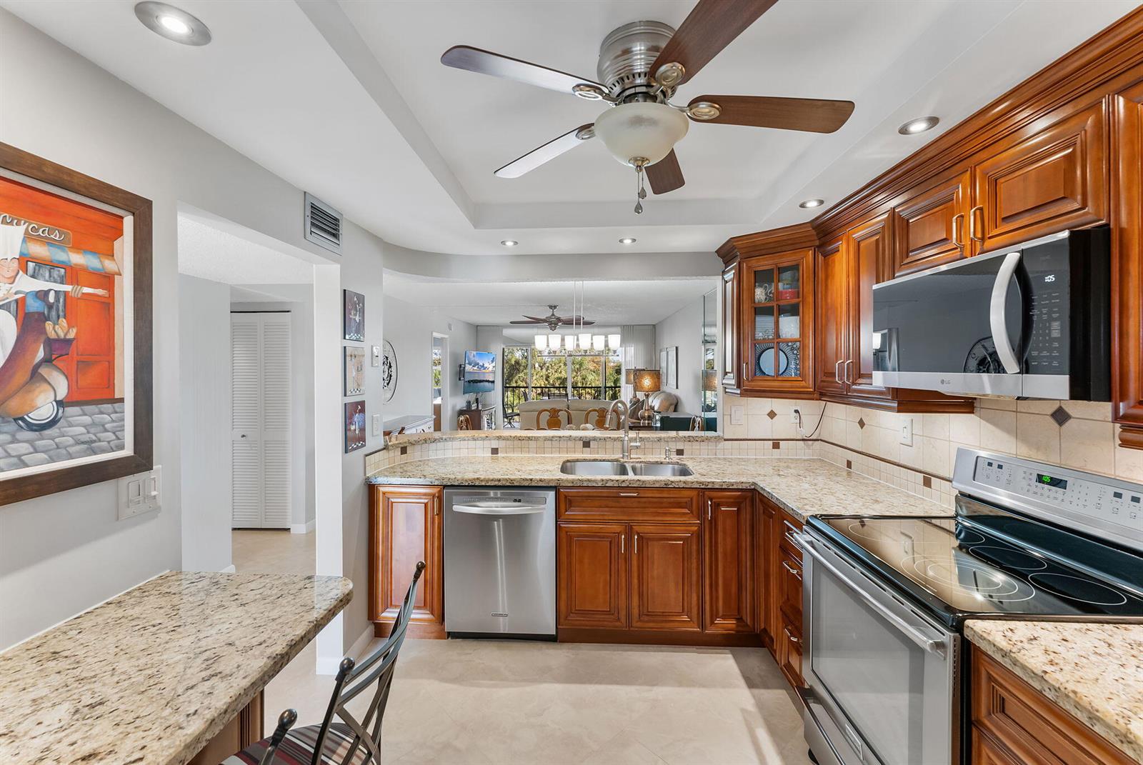 A kitchen with wood cabinets, granite countertops, stainless steel appliances, and a ceiling fan — 3930 Inverrary Boulevard # d, Lauderhill FL 33319, LAUDERHILL, FL