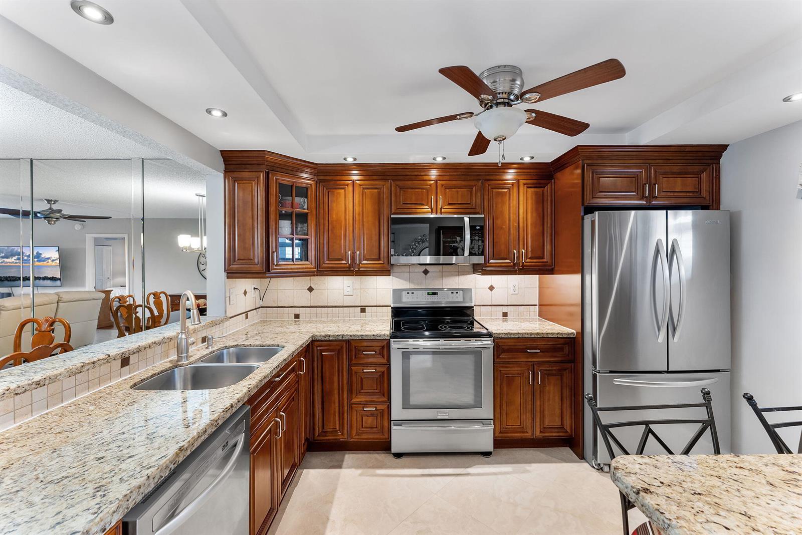 A kitchen with wood cabinets, granite countertops, stainless steel appliances, and a ceiling fan — 3930 Inverrary Boulevard # d, Lauderhill FL 33319, LAUDERHILL, FL