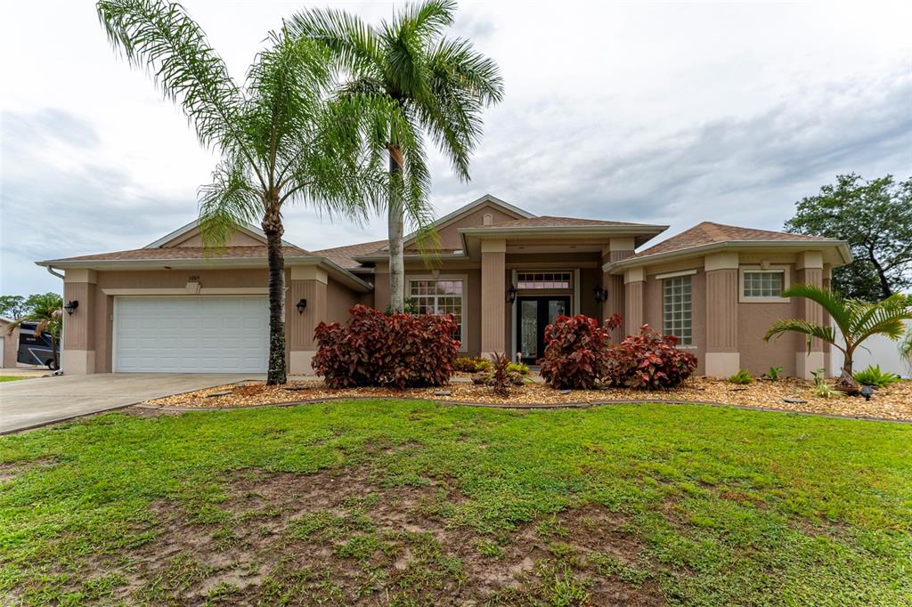 A tan single-story house features a two-car garage, a palm tree, and landscaped front beds — 1009 CAMPBELL STREET, PORT CHARLOTTE, FL