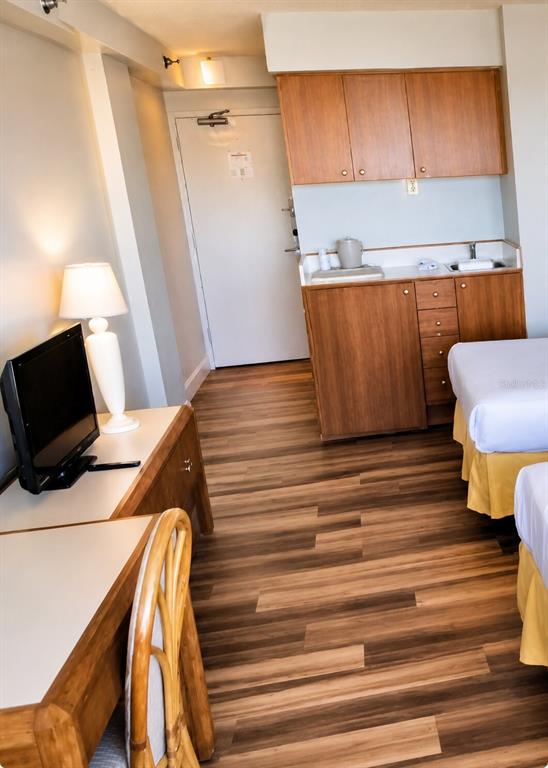 A hotel room features a kitchenette with wood cabinets, a desk with a television, and beds — 1909 S ATLANTIC AVENUE UNIT 714, DAYTONA BEACH, FL
