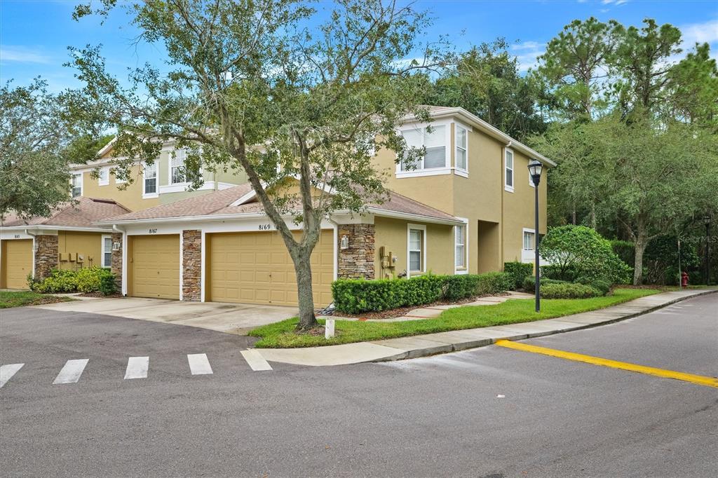 A two-story tan townhouse with a two-car garage and stone accents sits on a corner — 8169 STONE LEAF LANE, TAMPA, FL