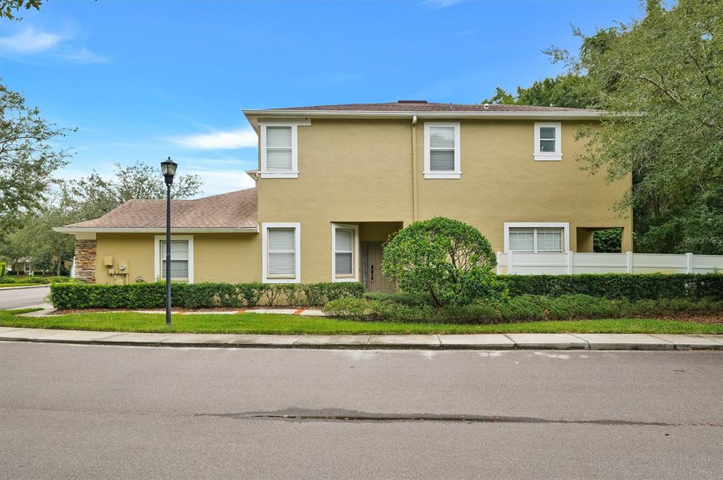 A two-story tan stucco house with a brown roof sits behind a manicured green hedge — 8169 STONE LEAF LANE, TAMPA, FL