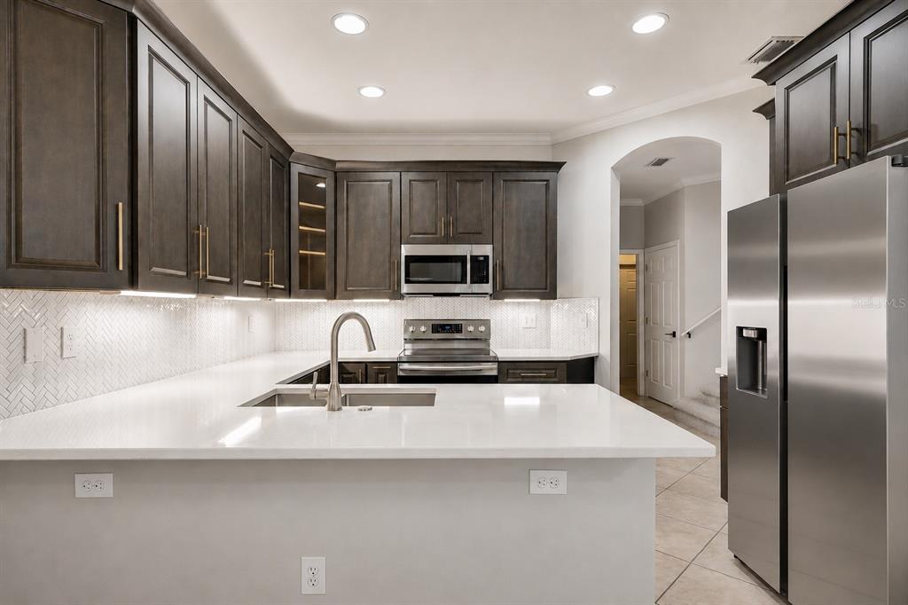 A modern kitchen features dark wood cabinets, white countertops, stainless steel appliances, and herringbone backsplash — 8169 STONE LEAF LANE, TAMPA, FL