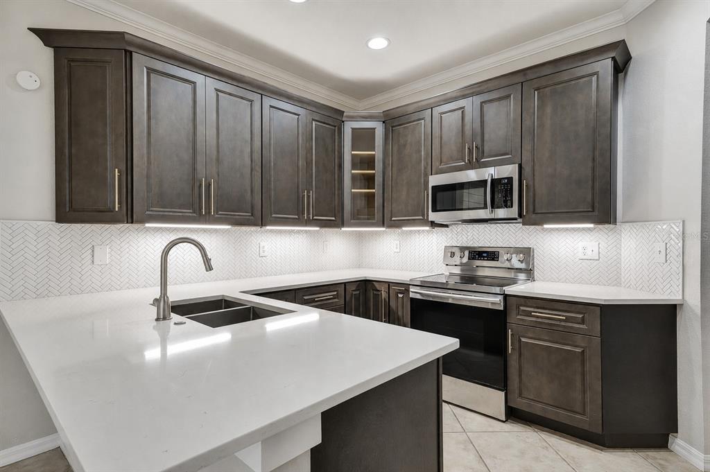 A kitchen features dark wood cabinets, white countertops, a herringbone backsplash, and stainless steel appliances — 8169 STONE LEAF LANE, TAMPA, FL