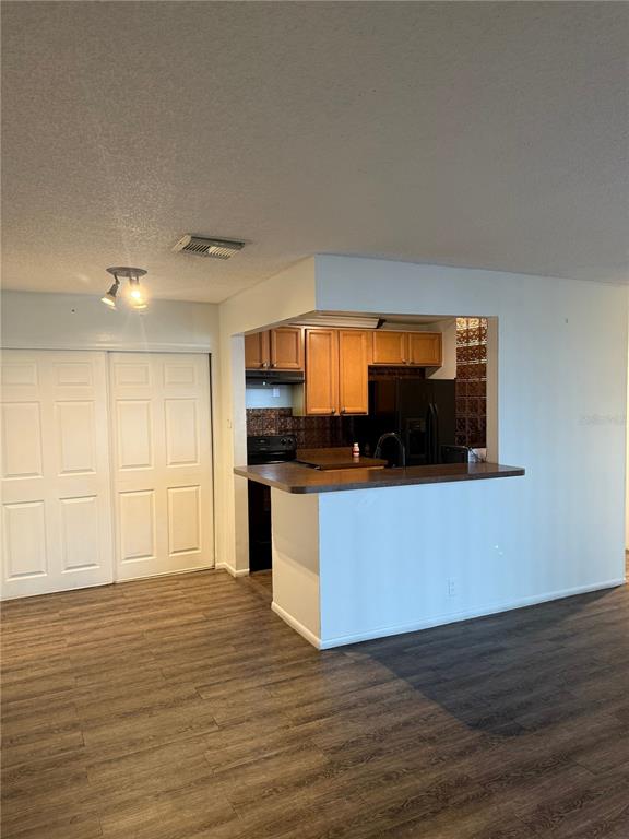 A kitchen with wood cabinets and a breakfast bar opens into a living area — 3827 BAY CLUB CIR UNIT 103, KISSIMMEE, FL