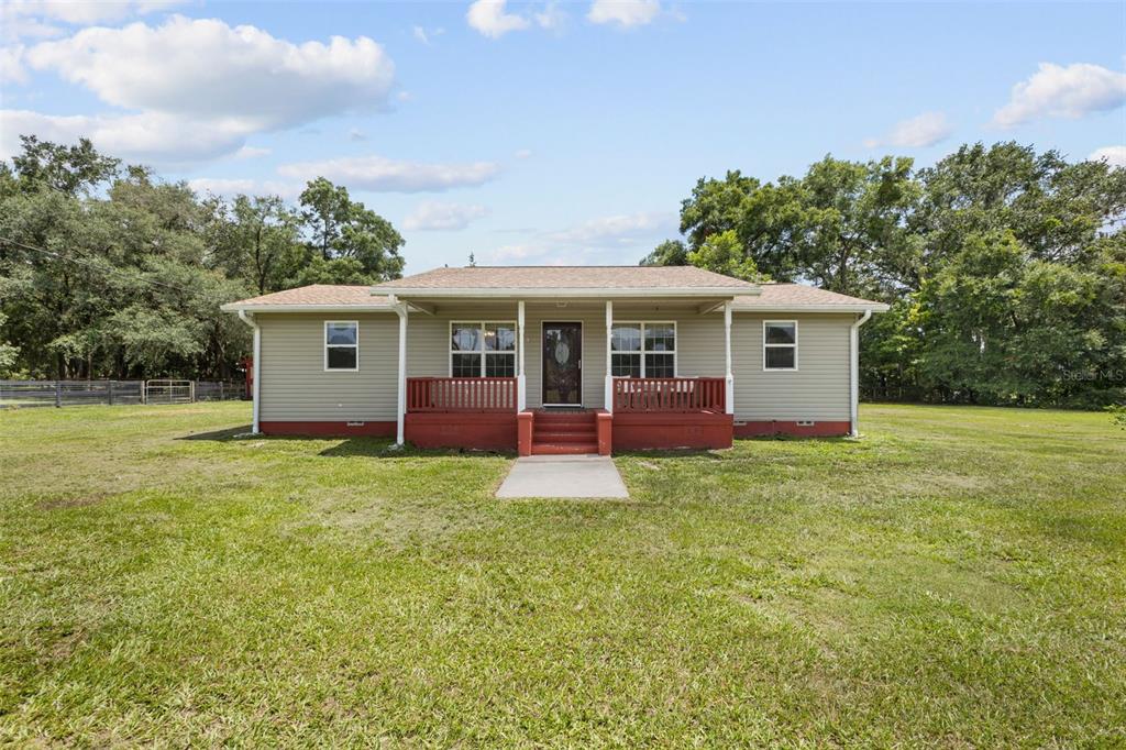 A single-story house with light-colored siding and a red front porch sits on a lawn — 18950 NE 55TH STREET, WILLISTON, FL