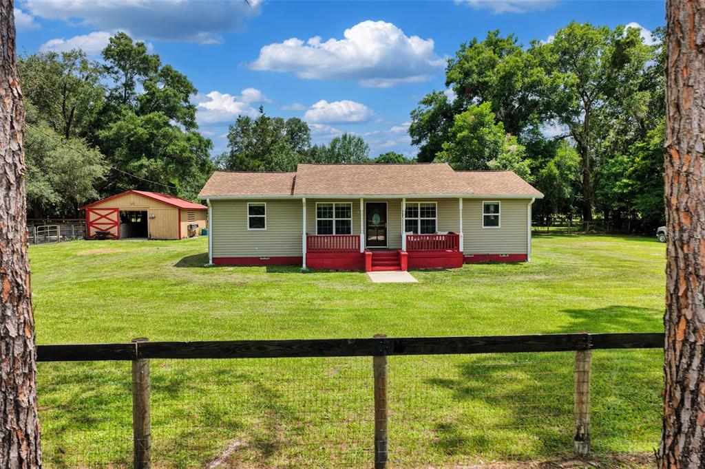 A tan single-story house with a red porch sits on a grassy lot with trees — 18950 NE 55TH STREET, WILLISTON, FL
